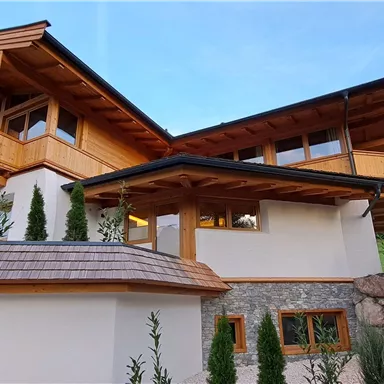 A modern wooden house with an inviting design. It is situated picturesque in a green setting.