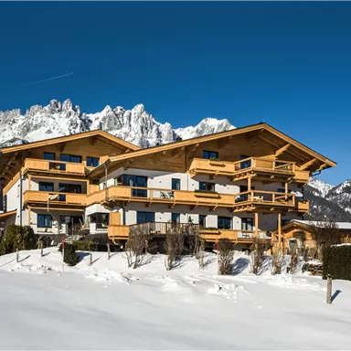 A modern chalet in the snow with a view of the mountains. The clear blue sky complements the winter landscape.