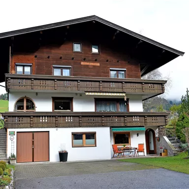 A traditional two-story house with wooden elements and a large balcony. The garden is well-maintained and there is a terrace with seating.