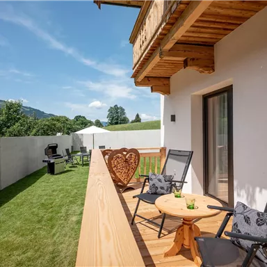 Ein schöner Balkon mit Holzbrüstung und Blick auf die grüne Landschaft. Zwei Stühle und ein Tisch laden zum Entspannen ein.