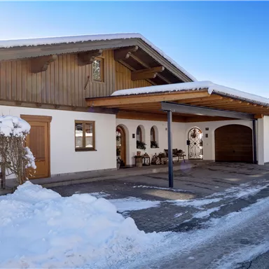 Ein modernes Haus im Schnee mit Holzverkleidung und Garagenplatz. Die Umgebung ist winterlich und einladend.