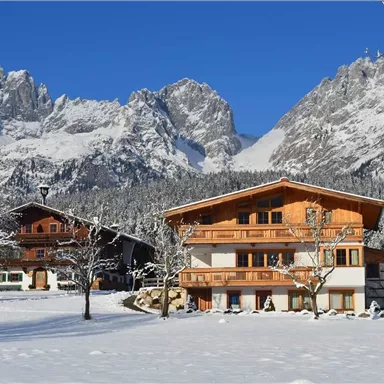 Ein malerisches winterliches Dorf mit schneebedeckten Bergen im Hintergrund. Die traditionellen Holzhäuser stehen umgeben von einer idyllischen Schneelandschaft.