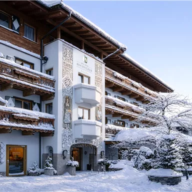 Ein charmantes Hotel im Winter mit schneebedeckten Balkonen und dekorativen Details. Die Umgebung ist ruhig und idyllisch, perfekt für einen entspannten Aufenthalt.