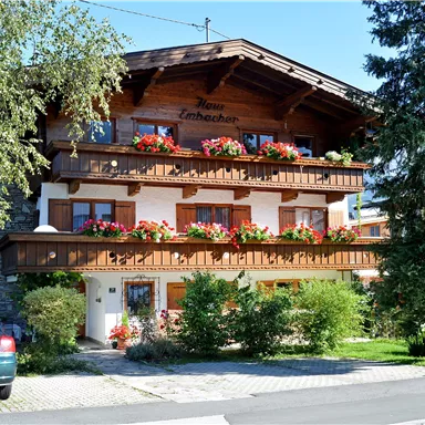 Ein charmantes Gebäude im Alpenstil mit blühenden Balkonkästen. Umgeben von einer grünen Landschaft und einem klaren blauen Himmel.