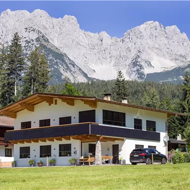 Ein modernes Haus mit einem schönen Garten, umgeben von Bergen und Bäumen. Der klare Himmel verleiht der Szene eine ruhige Atmosphäre.