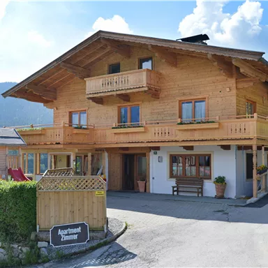 Ein schönes Holzhaus mit mehreren Balkonen und großen Fenstern. Umgeben von Grün und unter einem blauen Himmel.
