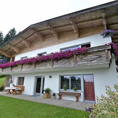 Ein hübsches Haus mit einem Balkon, der mit bunten Blumen geschmückt ist. Der Garten ist grün und lädt zum Entspannen ein.