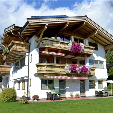 A beautiful chalet in alpine style with balconies and colorful flowers. In the background, mountains and a clear sky can be seen.