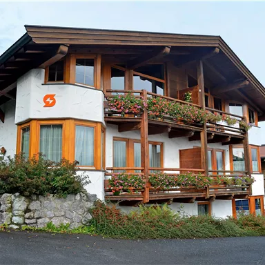 A charming building with wooden cladding and several balconies. Colorful flowers adorn the windows and the surroundings.
