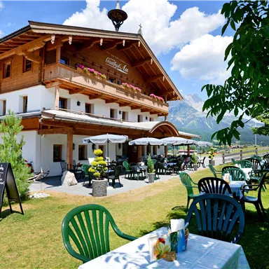 Ein charmantes Hotel im alpinen Stil mit einer einladenden Terrasse. Die grüne Wiese und der klare Himmel schaffen eine angenehme Atmosphäre.