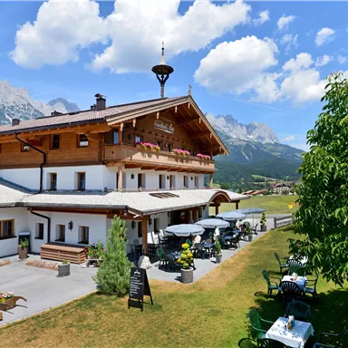 Ein malerisches Gebäude in den Alpen mit einem schönen Außenbereich. Im Hintergrund sind beeindruckende Berge und blauer Himmel zu sehen.