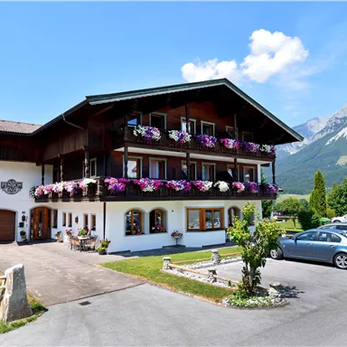 Ein charmantes Gebäude im alpinen Stil mit blühenden Balkonkästen. Im Hintergrund sind majestätische Berge und ein blauer Himmel zu sehen.