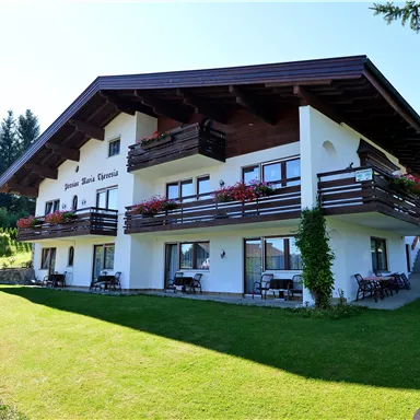 Ein gemütliches Haus mit einem großen Garten und Balkonen. Umgeben von grünen Bäumen und Bergen.