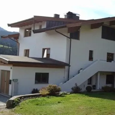 A beautiful house with two stories, surrounded by green countryside and mountains. It has a covered entrance and large windows.