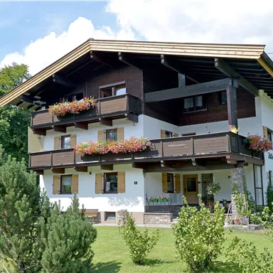 Ein hübsches Gebäude im landestypischen Stil mit Balkonen und Blumenkästen. Umgeben von grünen Wiesen und Bäumen.