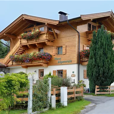 A charming wooden house with a balcony and colorful flower boxes. It is located in a picturesque setting with trees and a quiet street.