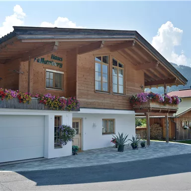 A cozy wooden house with colorful flowers and large windows. The surroundings are green and inviting.