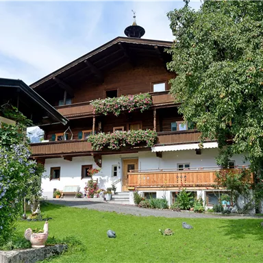 A traditional country house with a beautiful garden. The sky is clear and the surroundings are green and inviting.