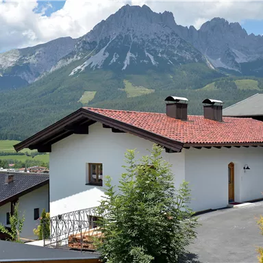A beautiful house with a red roof and a view of the mountains. The landscape is green and picturesque.