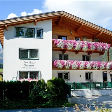 Ein schönes Alpenhaus mit bunten Blumenkästen. Im Hintergrund sind Berge und ein klarer Himmel zu sehen.