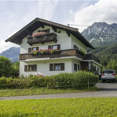 Ein gemütliches Haus in den Bergen mit blühenden Balkonen. Umgeben von grünen Wiesen und majestätischen Bergen.