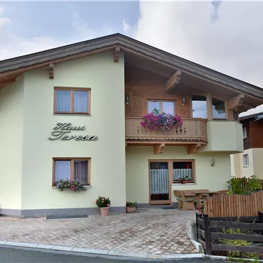 A beautiful house with a balcony and flowers. The surroundings are green and rural.