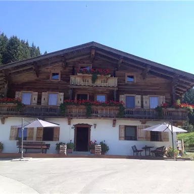 Ein traditionelles Holzhaus mit Balkonen voller Blumen. Es befindet sich in einer malerischen ländlichen Umgebung mit grünen Hügeln.