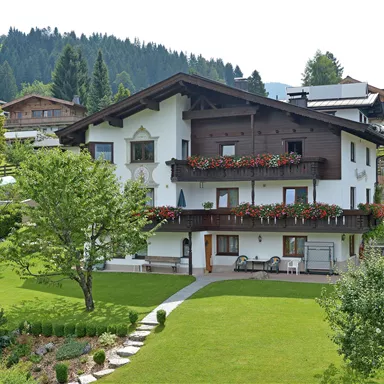 Ein charmantes Haus im alpinen Stil, umgeben von grünen Wiesen und Bäumen. Die Terrasse ist mit blühenden Blumen geschmückt.
