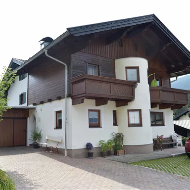 Ein schön gestaltetes zweigeschossiges Haus mit einem Balkon. Die Umgebung ist gepflegt mit Rasen und Blumen.