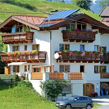 A beautiful house in alpine style with several balconies and flowers. It is set in a green environment with a view of the mountains.