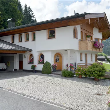 Ein charmantes Haus im alpinen Stil mit einem begrünten Außenbereich. Umgeben von Bäumen und einer malerischen Landschaft.