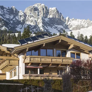 Ein modernes Chalet in den Bergen mit schneebedeckten Gipfeln im Hintergrund. Die Architektur kombiniert Holz und große Fenster, die viel Licht bringen.