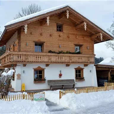 Ein schönes Holzhaus im Alpenstil, umgeben von schneebedeckter Landschaft. Es hat einen Balkon und eine gemütliche Atmosphäre.