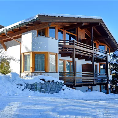 A cozy chalet in the mountains, surrounded by snow. The clear sky and sunny atmosphere create an inviting winter landscape.
