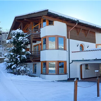 A modern house in the snow, surrounded by coniferous trees. The large window front lets in plenty of light.