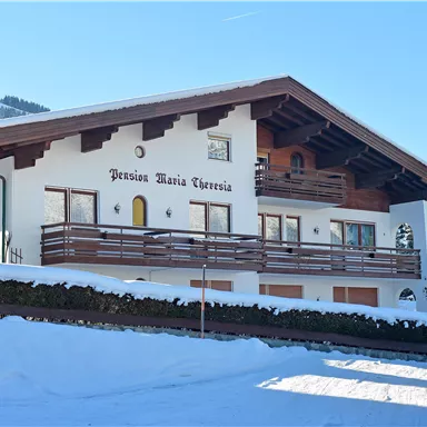 A charming house in alpine style, surrounded by snow. It has a large balcony and is surrounded by picturesque mountains.