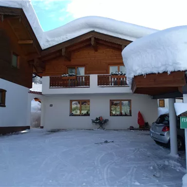 A cozy vacation home in the snow with a wooden design. The driveway is covered in snow and a car is ready.