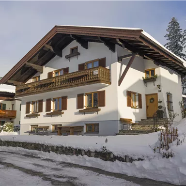 A traditional house in the snow with a balcony and wooden windows. The surroundings are wintry and peaceful.