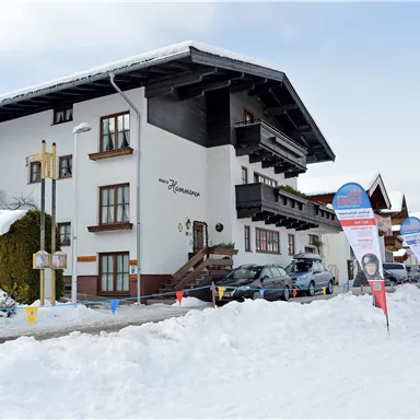 Ein großes Haus mit mehreren Etagen, umgeben von Schnee. Im Vordergrund stehen Werbeschilder und ein Schneemobil.