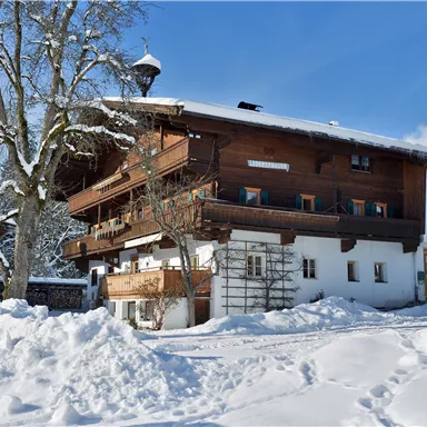 A traditional wooden house in the snow with a clear blue sky. Surrounding it is a dreamy winter landscape.