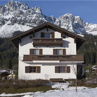 A charming house surrounded by snow-covered mountains. The clear blue sky gives the scene a calm atmosphere.