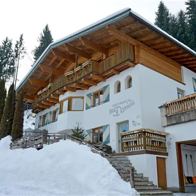 Ein gemütliches Chalet mit Holzbalkonen, umgeben von verschneiten Bäumen. Die Architektur vereint traditionelle und moderne Elemente in einer malerischen Winterlandschaft.