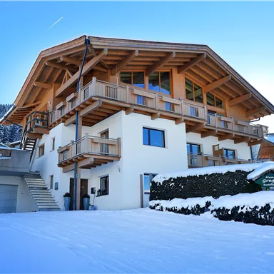 Ein schönes Holzhaus im Winter, umgeben von Schnee. Die blauen Fenster und Balkone verleihen dem Gebäude einen einladenden Charakter.