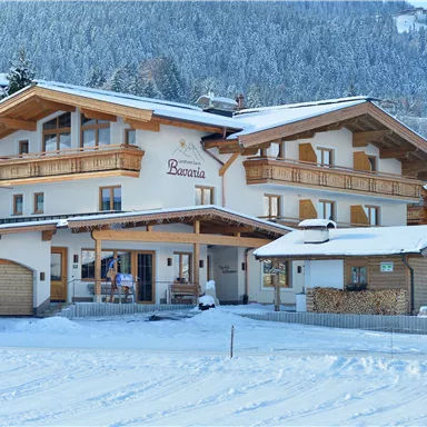 Ein gemütliches Holzhaus im winterlichen Schnee. Die Umgebung ist von verschneiten Bäumen und Bergen umgeben.
