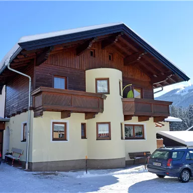 A two-story house with a wooden-clad upper floor.
It is located in a snowy environment and has a clear blue sky in the background.