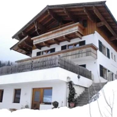 Ein modernes Haus im alpinen Stil, umgeben von Schnee. Die Architektur kombiniert Holz- und Betonelemente und hat große Fenster.