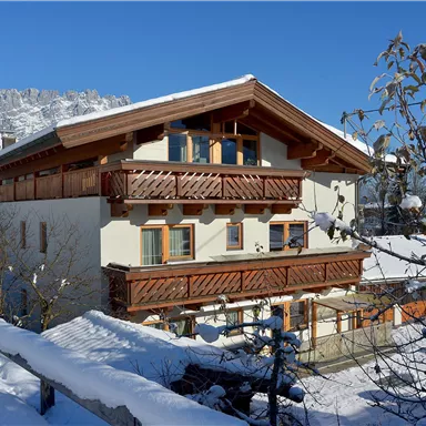 A cozy chalet in the snow, surrounded by mountains. The bright blue sky and fresh snow give the landscape an idyllic atmosphere.