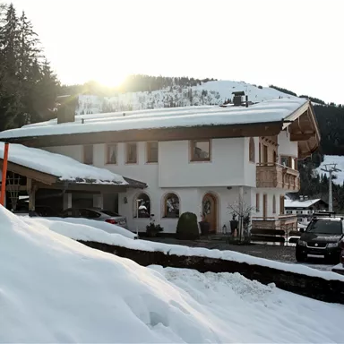 Ein charmantes Chalet im Schnee mit Bergen im Hintergrund. Die Sonne scheint sanft auf das Gebäude und die Umgebung.