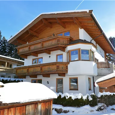 A modern chalet in the mountains, surrounded by snow. The architecture blends wood and plaster with large windows for plenty of light.