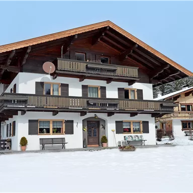 A large, rustic chalet in the snow, surrounded by a wintry landscape. The sky is clear and the surroundings are peaceful.